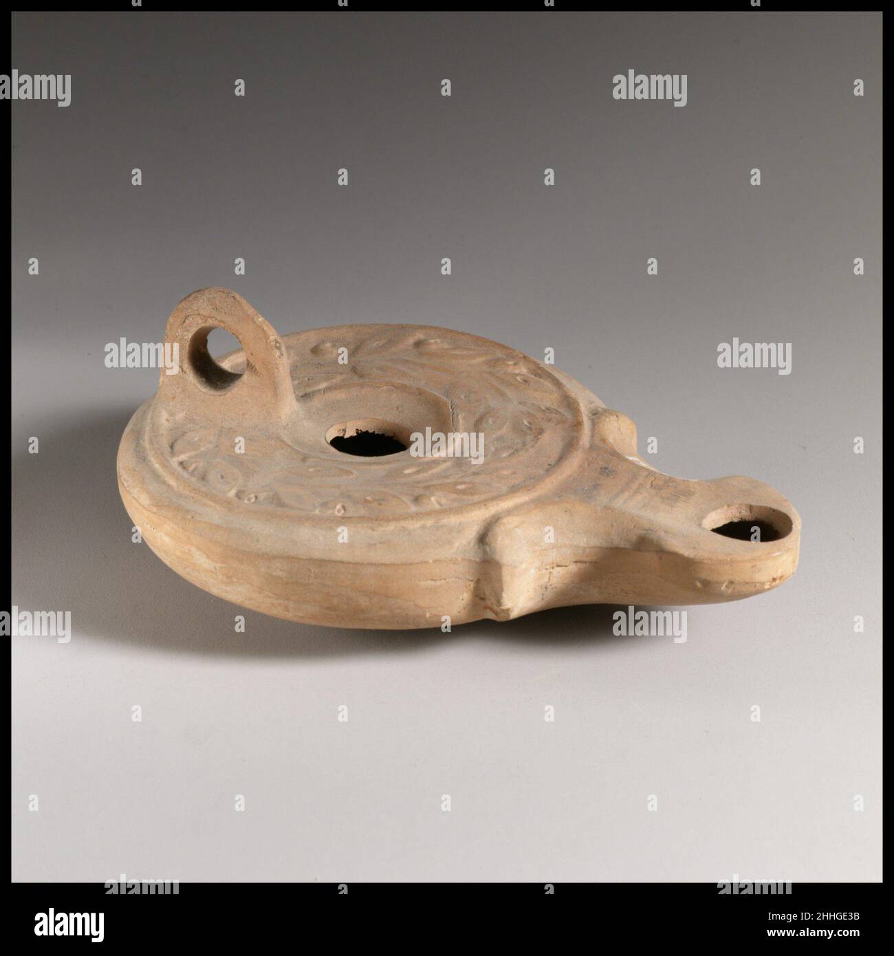 Terrakotta-Öllampe 3rd Jahrhundert A.D. römische Form-gebildet, mit durchbohrtem Griff. Kleiner, leicht konkaver Diskus mit einem großen zentralen Einfüllloch; eine breite, horizontale Schulter, flankiert von zwei erhöhten Kreisen, reliefverziert mit einem Kranz aus Blättern und Beeren. Spiraldüsen flankieren leicht eckige Düse, mit zwei kleinen parallelen Linien über die Oberseite der Düse zwischen den Spiraldüsen. Angehobener Sockelring und flach base.Complete, mit Ausnahme eines großen Lochs im Sockel. Terrakotta-Öllampe 241502 Stockfoto