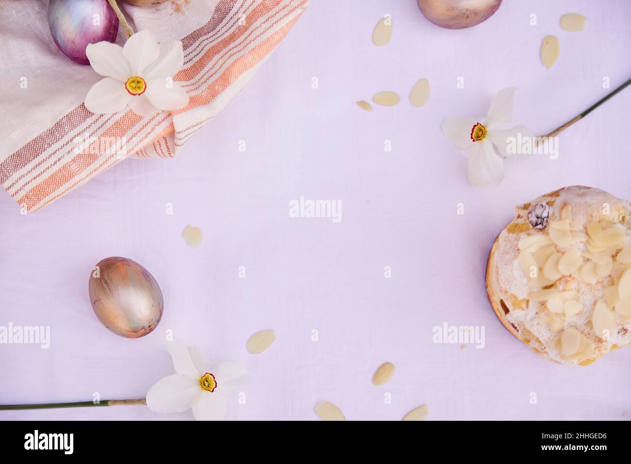 Ostern eleganter Hintergrund. Violette Vintage- und orangefarbene bunte Eier, Narzissenblüten und Mandelflocken. Hausgemachter Osterkuchen. Draufsicht, Kopierbereich. Stockfoto