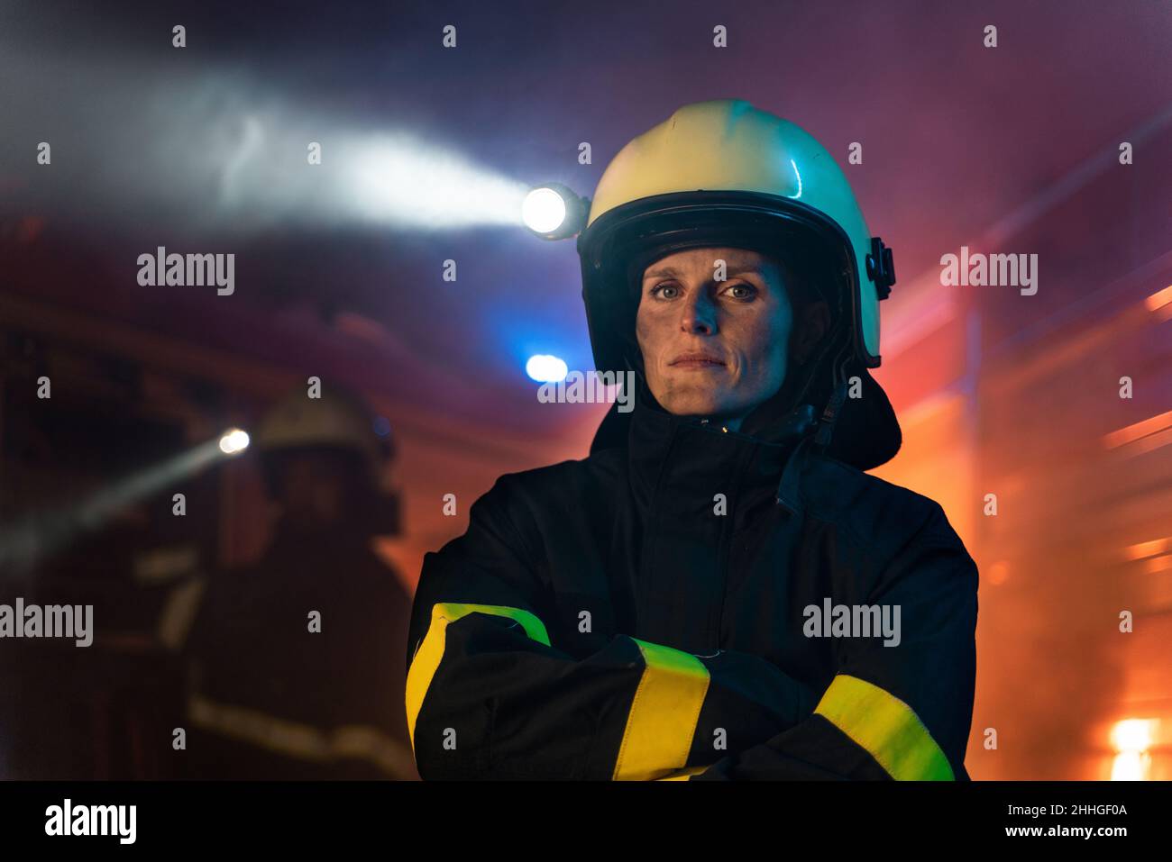 Schmutzige Feuerwehrfrau, die nachts mit einem Feuerwehrauto im Hintergrund auf die Kamera schaut. Stockfoto