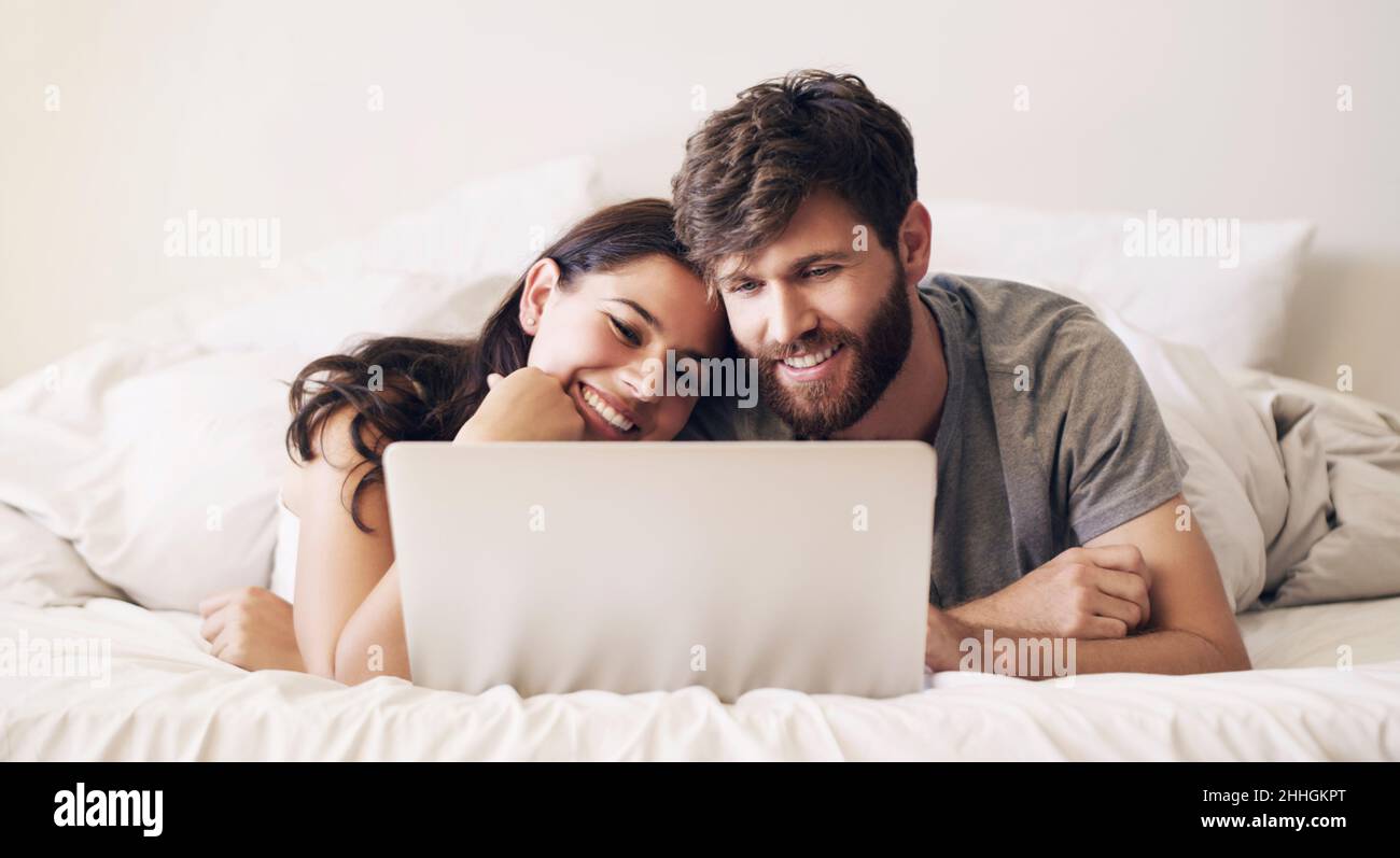 Sparen Sie sich jeden Tag Zeit, um eine Verbindung herzustellen. Aufnahme eines glücklichen jungen Paares, das einen Laptop benutzt, während es sich zu Hause auf dem Bett entspannt. Stockfoto