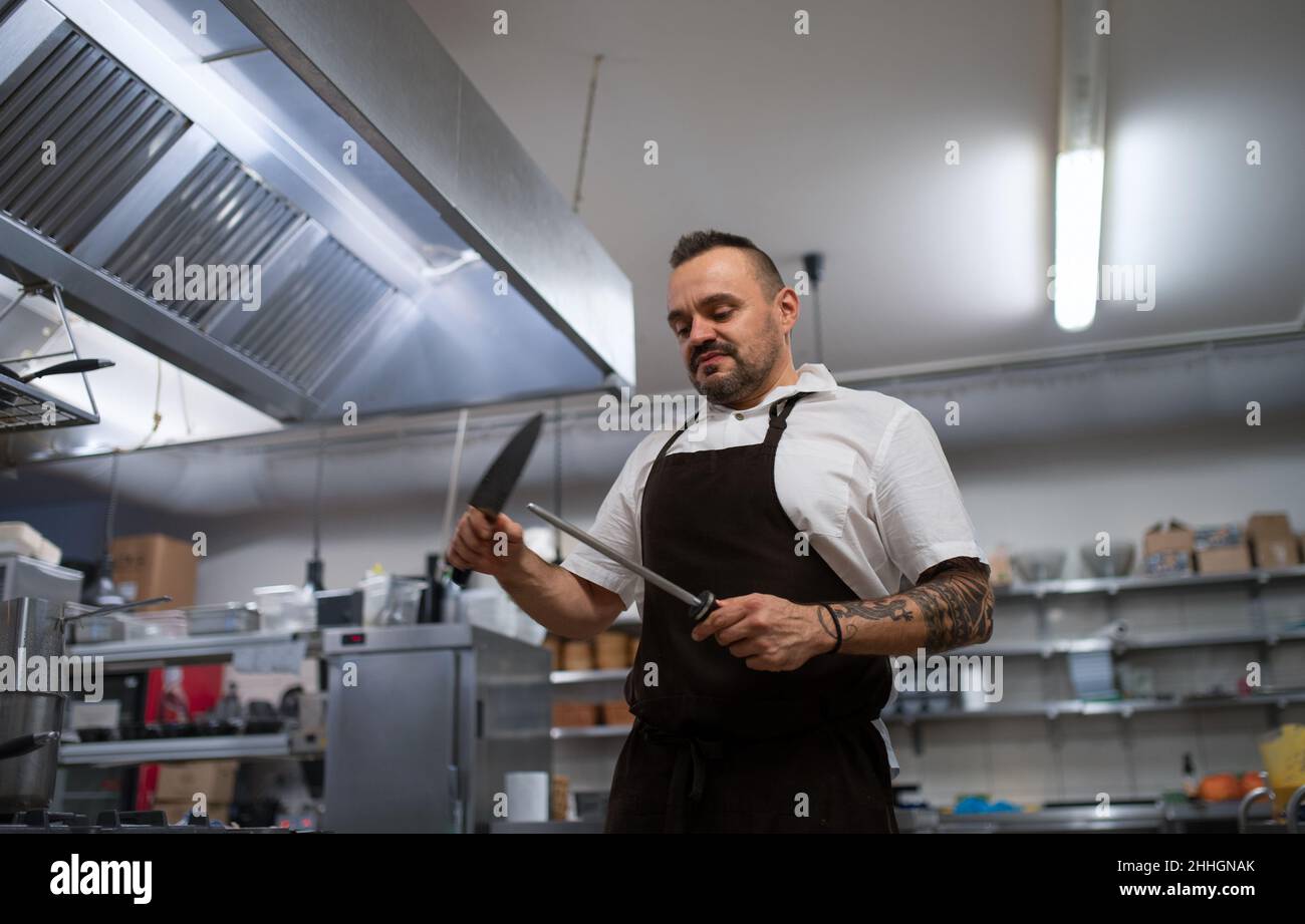 Niedriger Winkel Ansicht des professionellen Küchenchefs, der Messer in der Restaurantküche schärft. Stockfoto