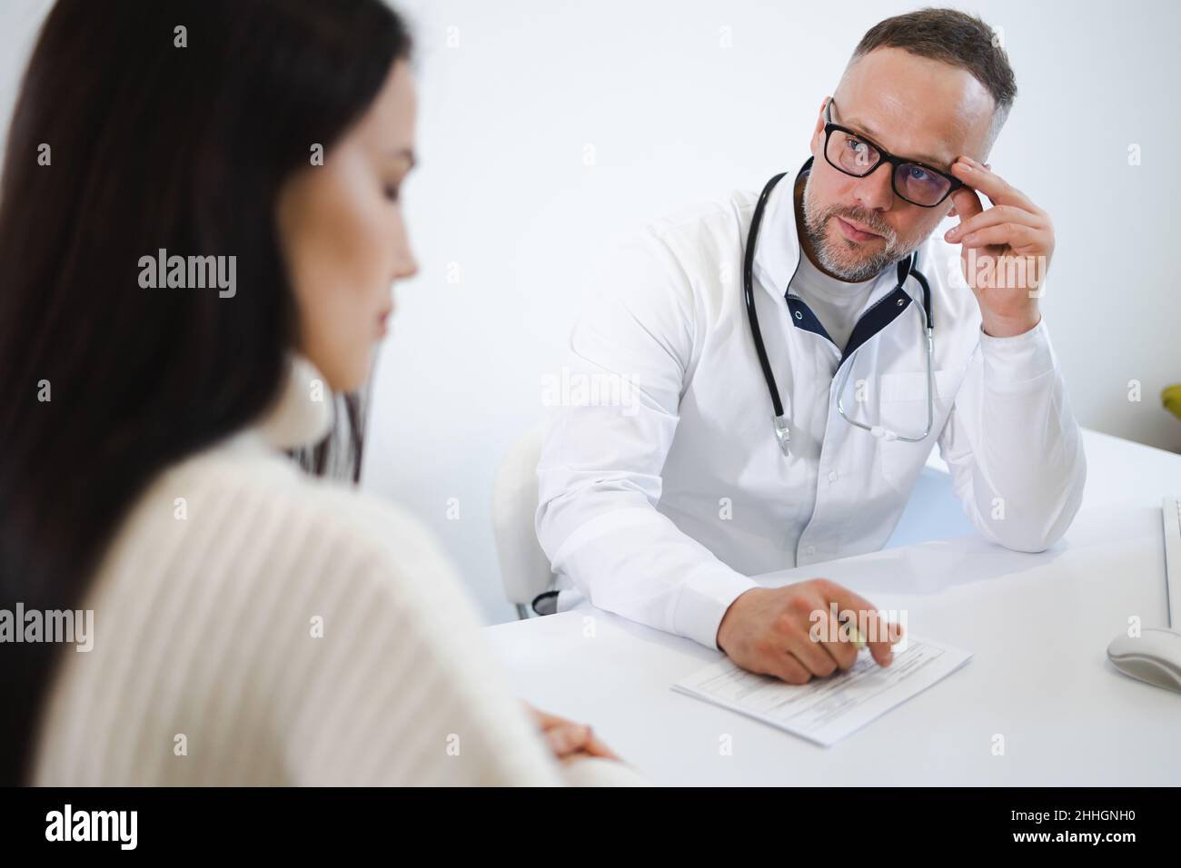 Männlicher Arzt fragt Frau über gesundheitliche Beschwerden während der körperlichen Untersuchung. Patient in der Arztpraxis Stockfoto