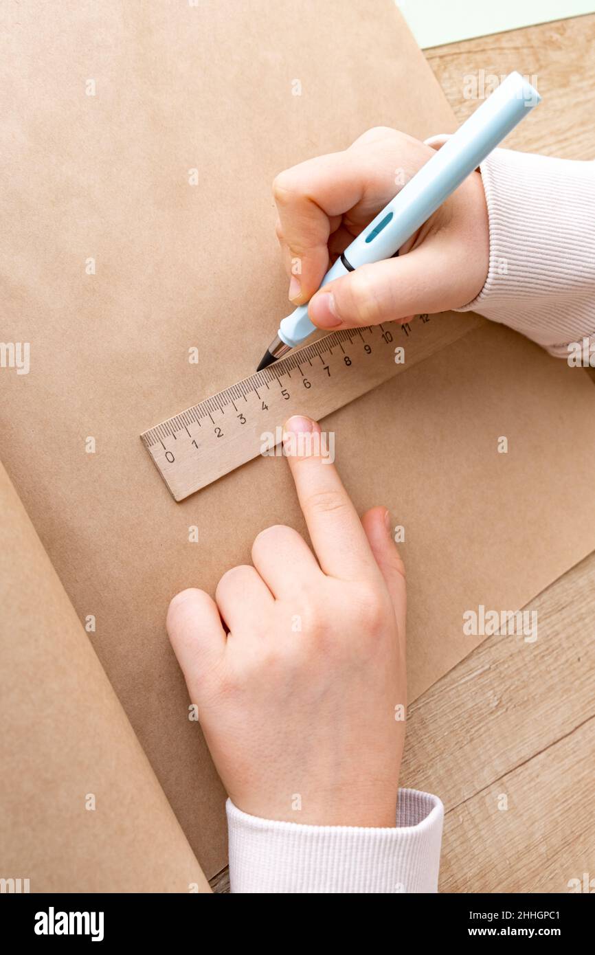 Nahaufnahme von Kinderhänden, die mit Bleistift auf Bastelpapier skizziert werden. Schulkind oder Vorschulkinder, die Hausaufgaben machen. Gerade Linie mit Lineal Stockfoto