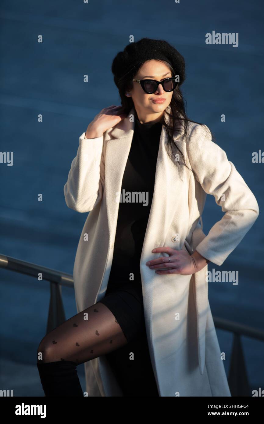 Ein beautfiul weibliches Modell mit langen dunklen Haaren, Hut und Sonnenbrille, weißem Mantel, natürlich posiert in der berühmten Gae Aulenti, Mailand, Italien Stockfoto