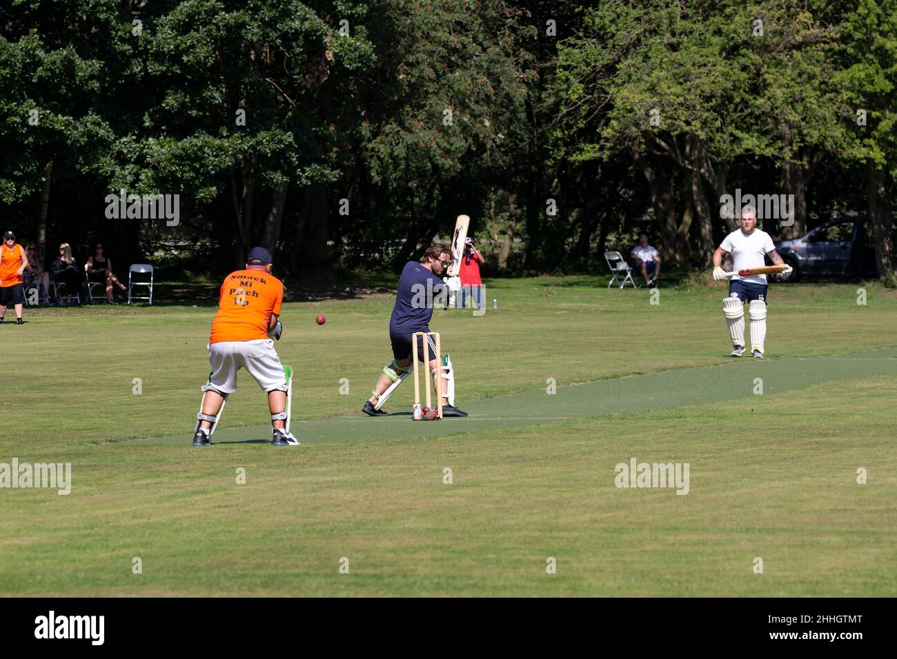 Eine Sommerszene am Wochenende, in der Amateur-Cricketspieler ein Knockout-Spiel auf einem von Bäumen gesäumten Boden genießen Stockfoto