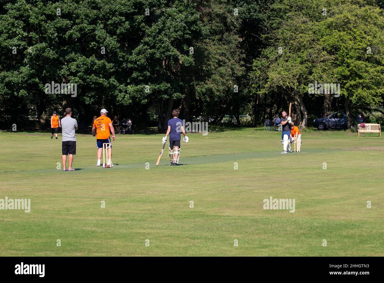 Eine Sommerszene am Wochenende, in der Amateur-Cricketspieler ein Knockout-Spiel auf einem von Bäumen gesäumten Boden genießen Stockfoto