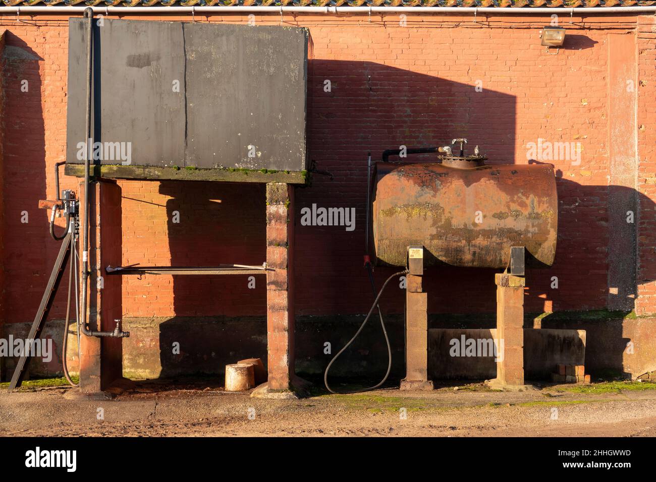 Tankstelle und Öltank auf dem Hof. Ein rechteckiger und ein zylindrischer gegen eine Scheunenwand mit schweren grafischen Schatten Stockfoto