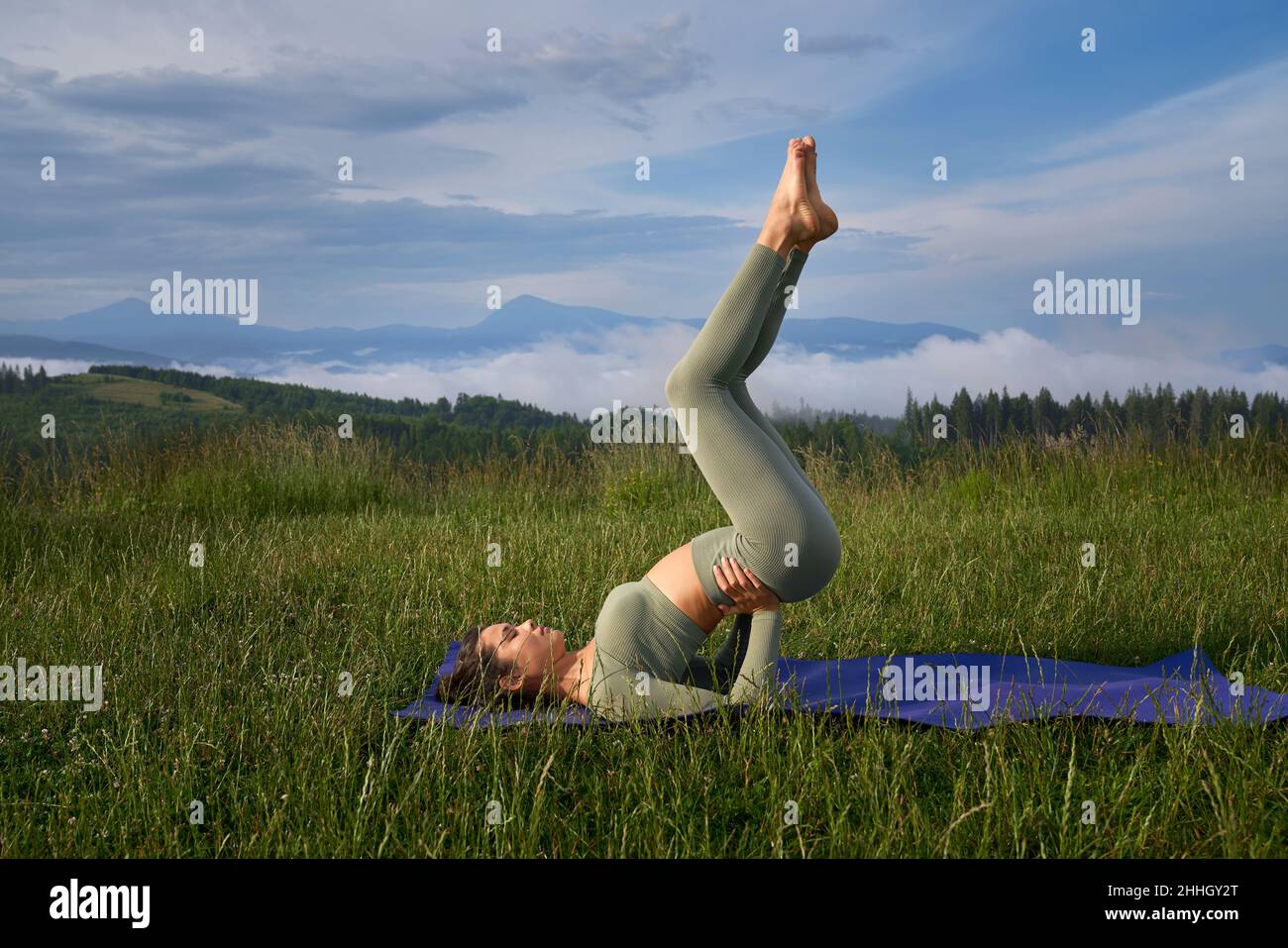 Junge Frau, die während des aktiven Trainings an der frischen Luft Gleichgewichtsübungen praktiziert. Weibliche Person, die morgens Zeit für das Training in den Sommerbergen verbringt. Stockfoto