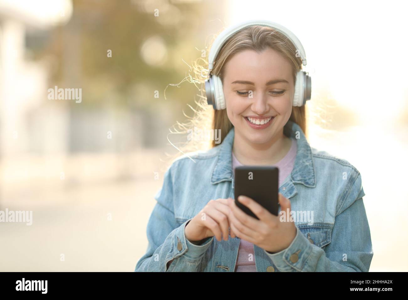 Vorderansicht eines glücklichen Teenagers, der Kopfhörer trägt und Musik hört, die im Freien läuft Stockfoto