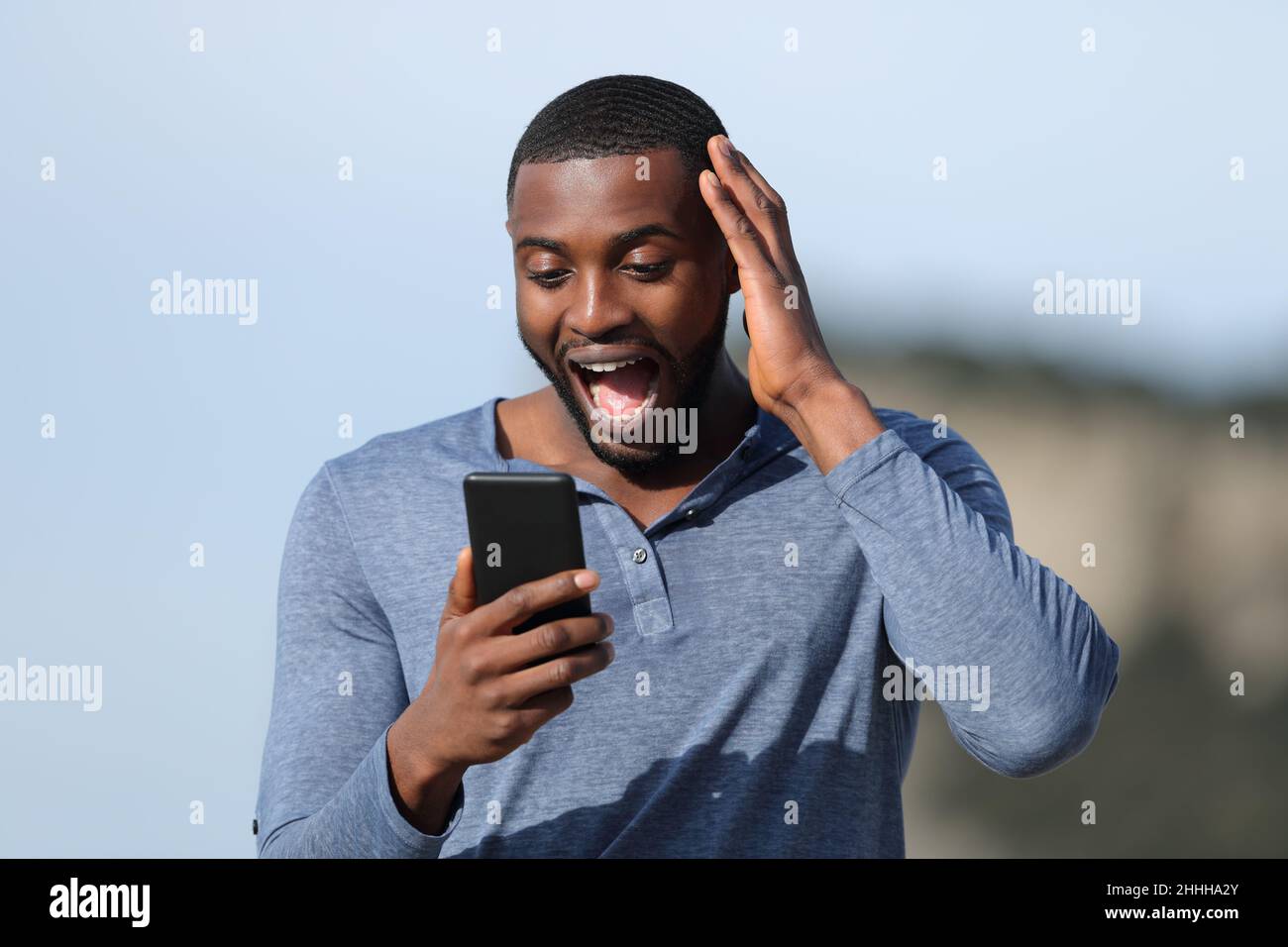 Staunender Mann mit schwarzer Haut überprüft Smartphone im Freien einen sonnigen Tag Stockfoto