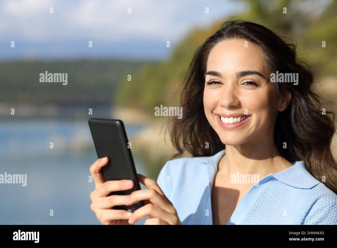Glückliche Frau mit Smartphone und Blick auf Sie in der Natur Stockfoto