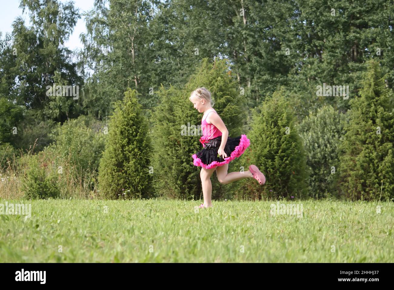 Liebenswert blonde Mädchen in einem Pettirock gekleidet spielen und laufen in einem Sommerpark auf dem Land. Stockfoto