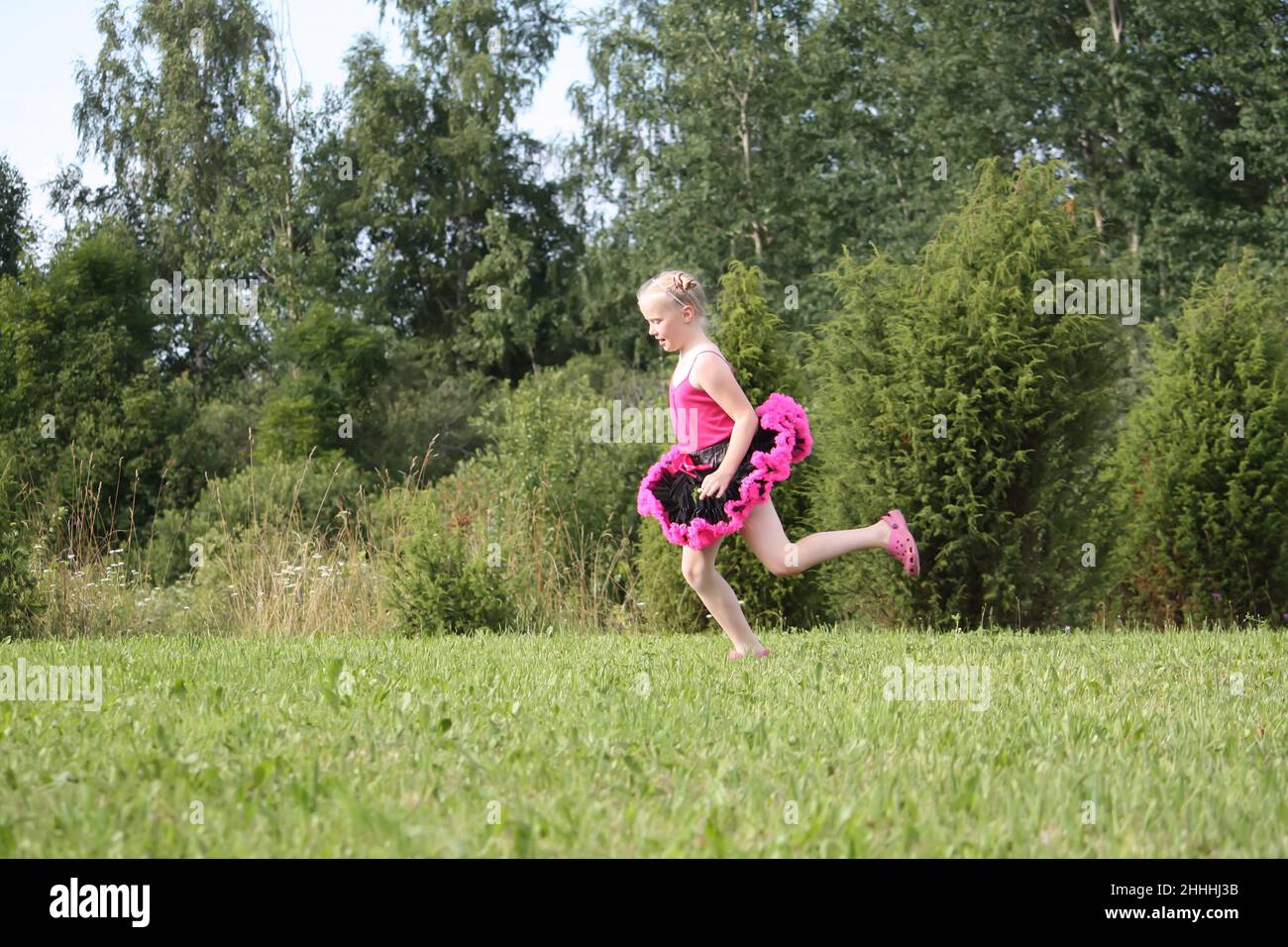 Liebenswert blonde Mädchen in einem Pettirock gekleidet spielen und laufen in einem Sommerpark auf dem Land. Stockfoto