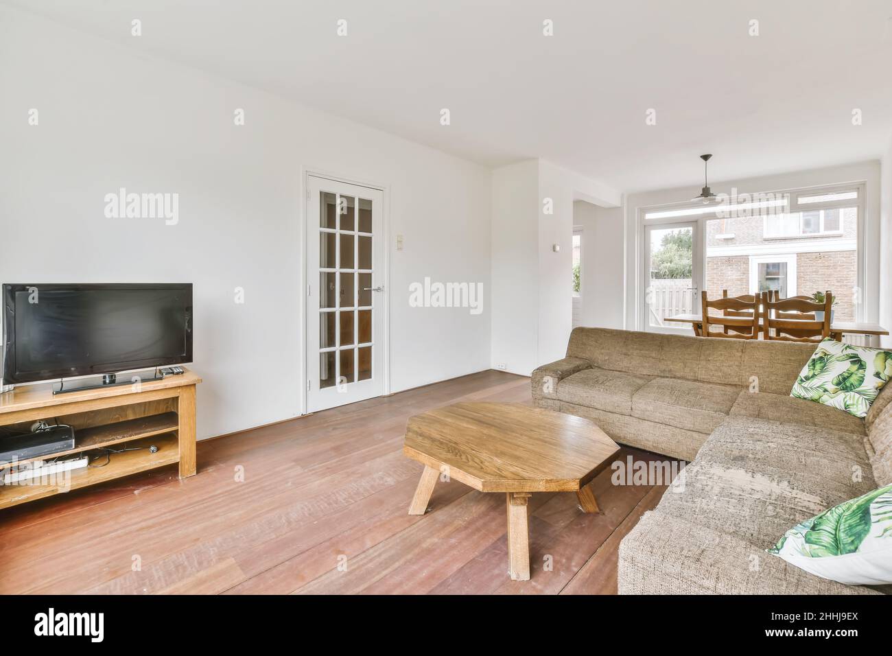 Blick auf das weiße Wohnzimmer in minimalistischem Stil mit Fernseher, Sofa, achteckiger Holztisch Stockfoto