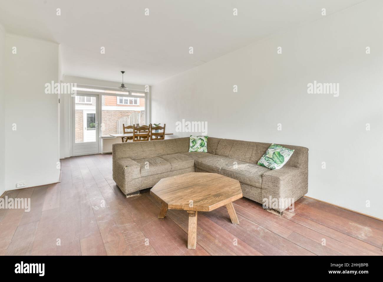 Blick auf das weiße Wohnzimmer in minimalistischem Stil mit Sofa, Kissen und einem achteckigen Holztisch Stockfoto