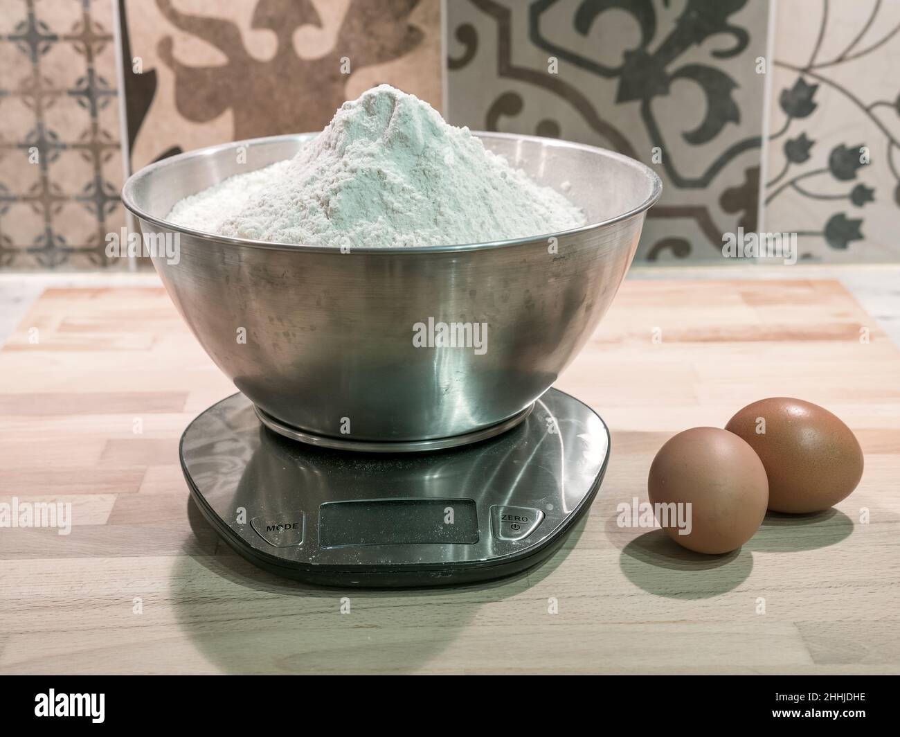 Zwei rohe Eier und ein Kilogramm Weizenmehl werden mit einer elektronischen Waage auf der Küchentifläche gewogen Stockfoto
