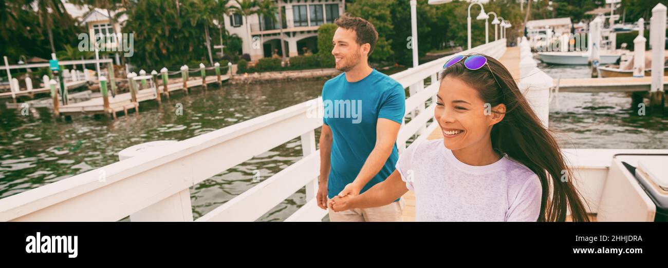 Glückliche junge Leute, die auf der Strandpromenade von Florida am Marina Harbour Pier spazieren gehen und sich die Hände halten. Interracial Beziehung Asiatisches Mädchen, kaukasischer Mann Stockfoto