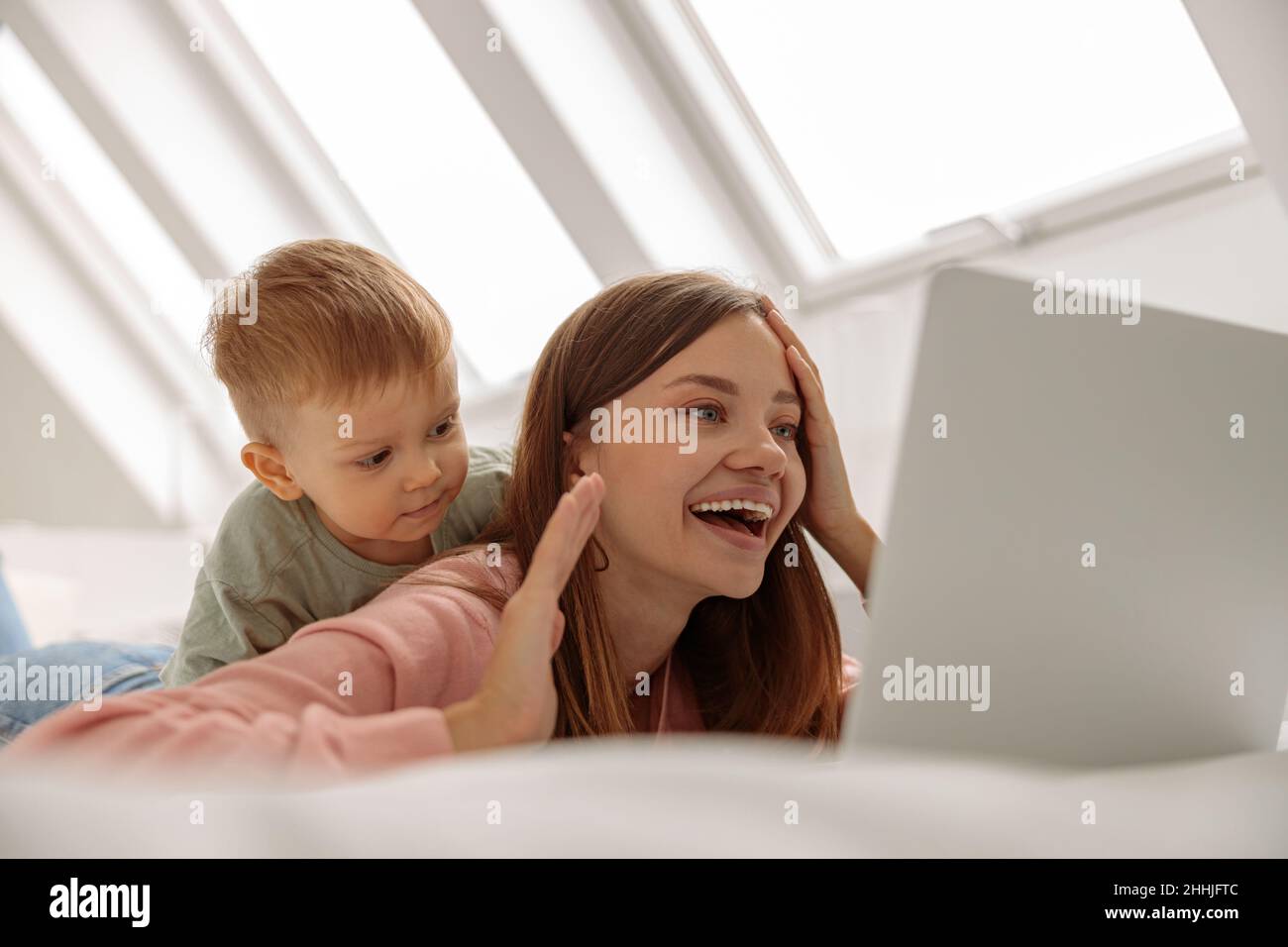 Lächelnde junge Mutter mit Laptop, während sie Zeit mit ihrem Baby verbringt Stockfoto