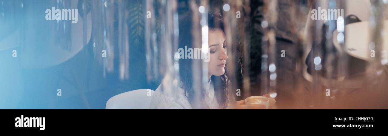 Frau trinkt im Winter Kaffee im Café. Verträumt entspannt erwachsenen Weibchen in ihrem 40s. Blick durch das Lametta. Reflexionen und Blendung Stockfoto