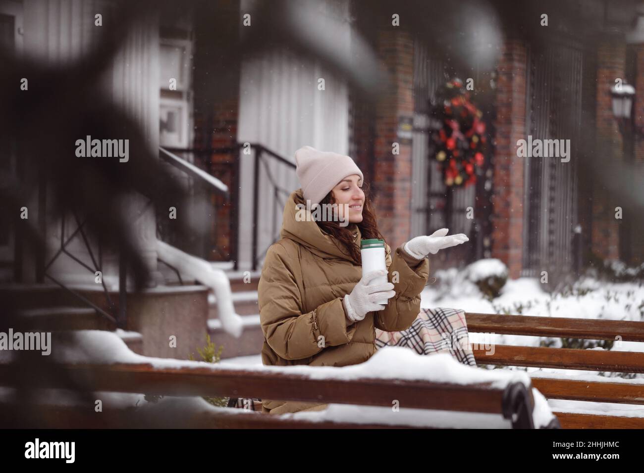 Fröhlich brünette Frau trinken aus Kolben im Freien in der Stadt im Winter. Aufwärmen, Momente genießen, Bremsen über schneebedeckten Bäumen Stockfoto