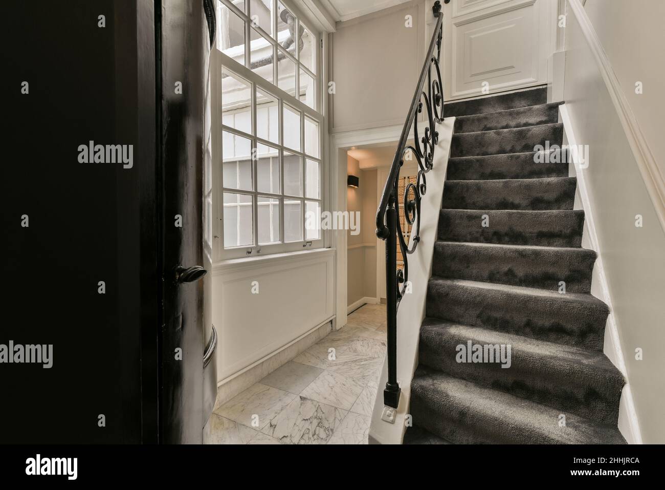 Inneneinrichtung des Hausflurs mit weißen Wänden und schwarzer Treppe in der Nähe des Fensters bei Tageslicht Stockfoto