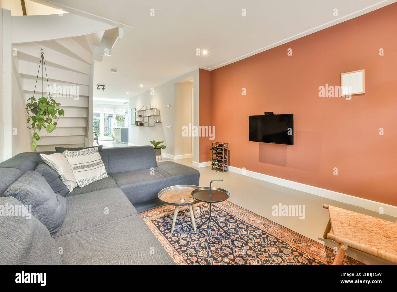 Bequemes Sofa mit Kissen an der roten Wand mit modernem Fernseher im hellen, stilvollen Wohnzimmer mit Fenstern in der Wohnung Stockfoto