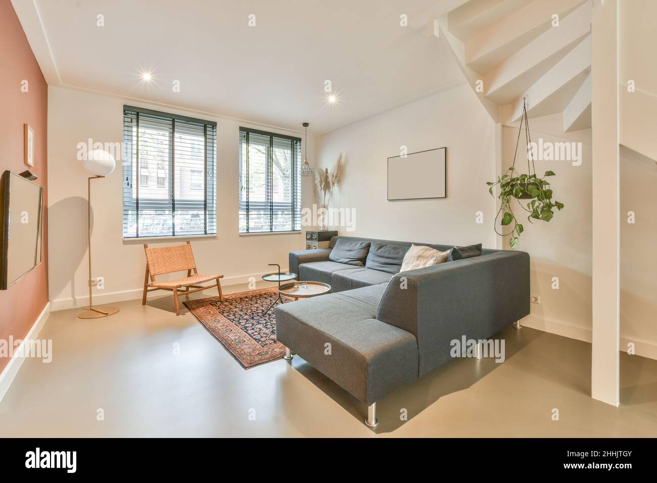 Bequemes Sofa mit Kissen an der roten Wand mit modernem Fernseher im hellen, stilvollen Wohnzimmer mit Fenstern in der Wohnung Stockfoto