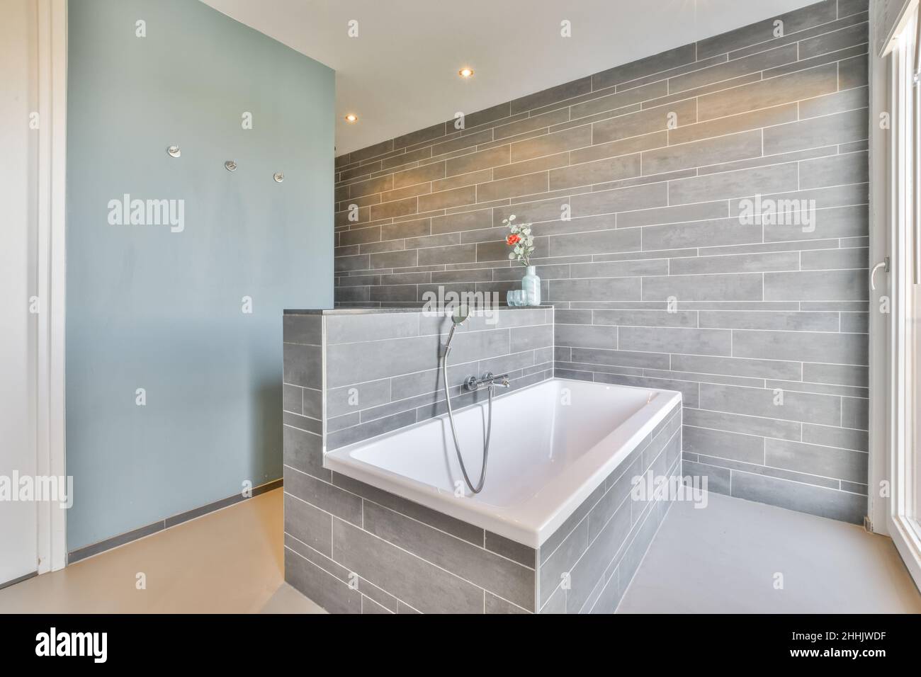 Interieur des modernen Badezimmers mit gefliesten Wänden und eingebauter Keramik-Badewanne in der Nähe des Fensters Stockfoto