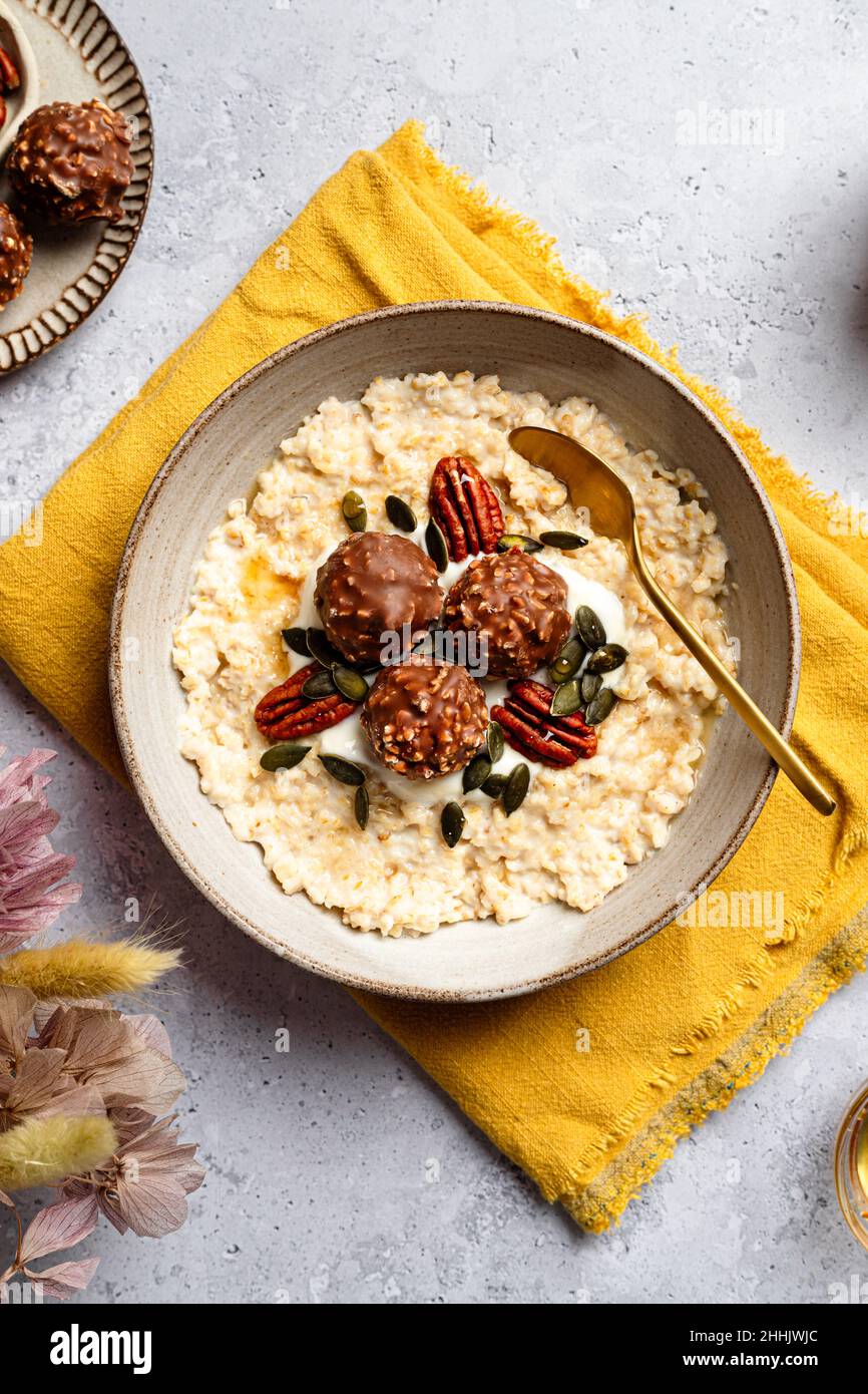 Hohe Winkel der Schüssel mit leckeren Milch Haferflocken serviert mit knusprigen Schokoladenkugeln Kürbiskerne und Pekannuss auf Serviette für ein gesundes Frühstück Stockfoto