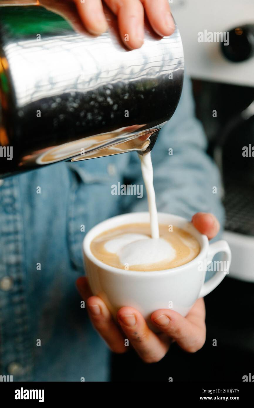 Ernte nicht erkennbaren Barista, gieße Milch aus dem Krug in eine Tasse frisch gebrühten Kaffee, während du während der Arbeit im Café Latte zubereitetst Stockfoto