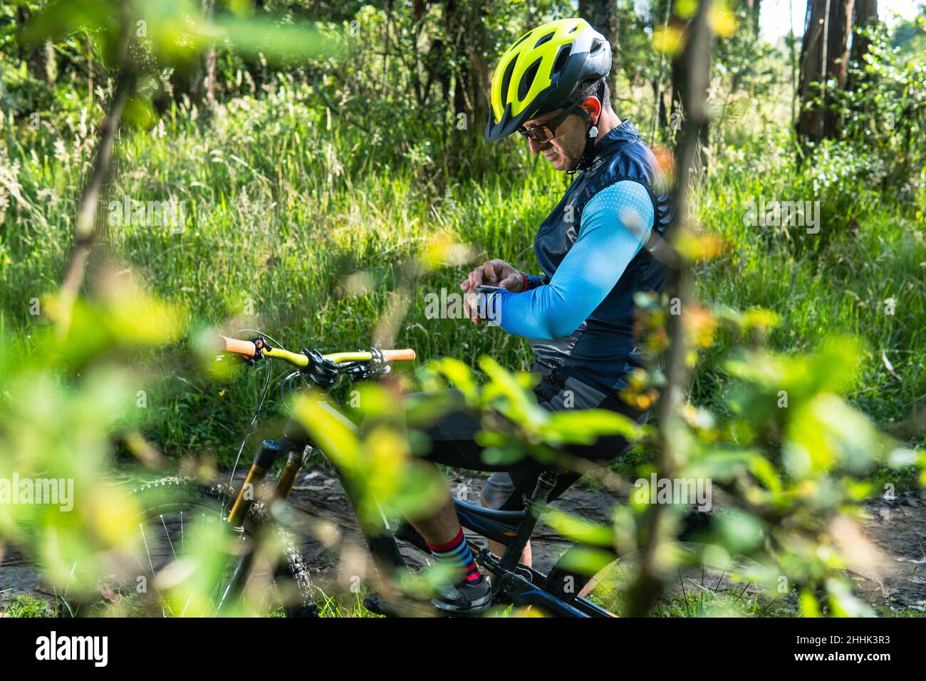 Ein Radsportler zwischen 30 und 40 Jahren beobachtet tagsüber in einem Wald seine smarte Uhr mitten auf dem Feld Stockfoto