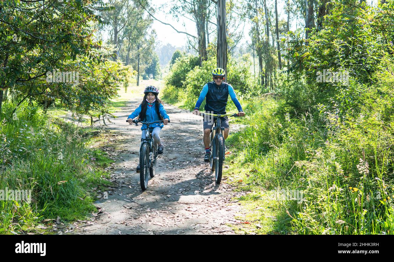 Ein Vater und eine Tochter fahren mit dem Mountainbike auf einer Landstraße im Wald Stockfoto