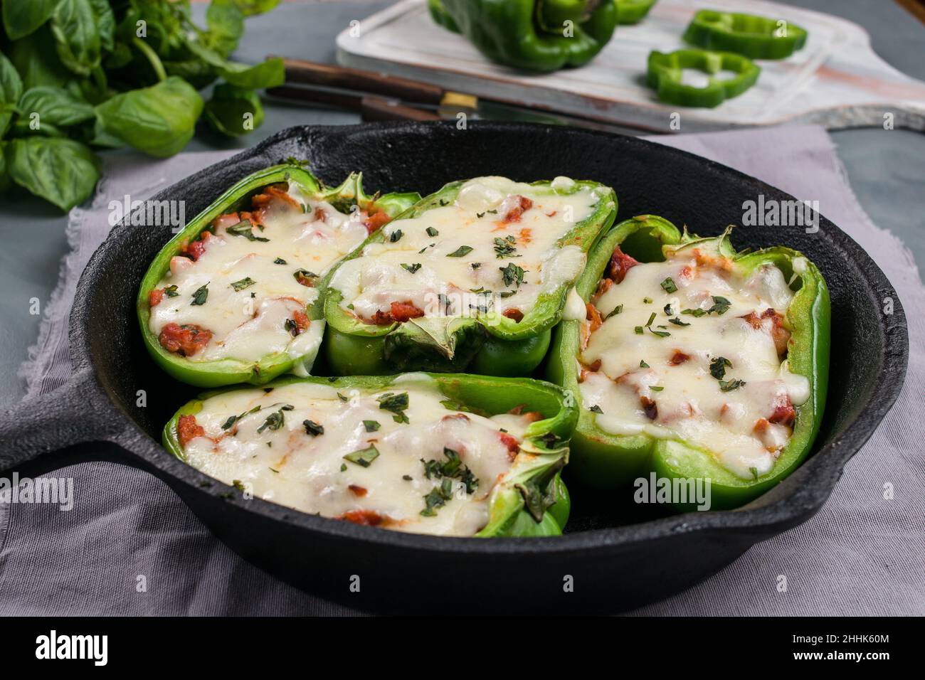 Hälften von grünem Paprika mit Pizzafüllung und geschmolzenem Käse in einer Pfanne auf dem Tisch mit grünen Kräutern in der Küche Stockfoto