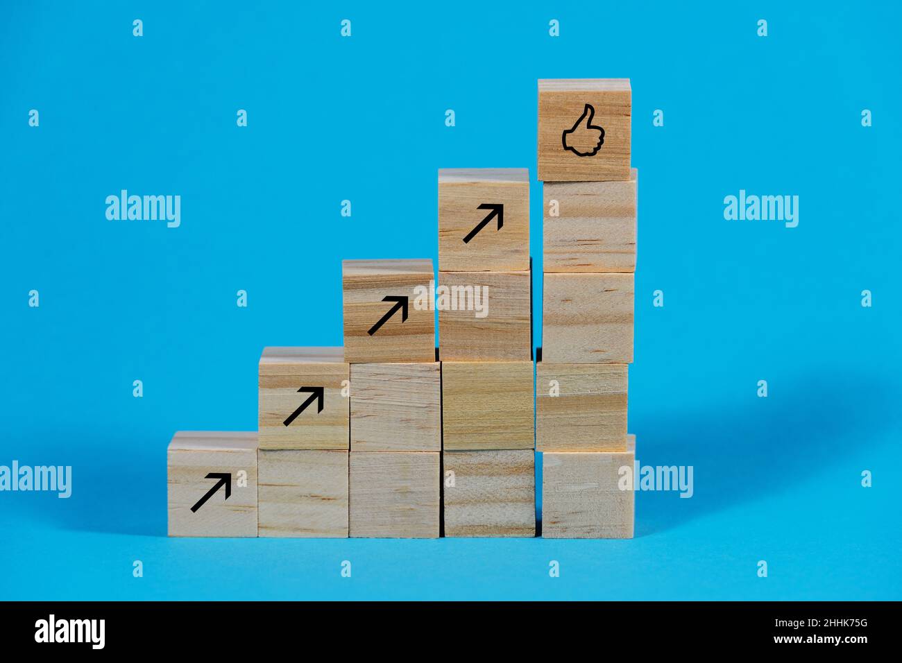 Holzwürfel als Treppenstufen mit Pfeilen nach oben und einem Daumen nach oben-Symbol auf der Oberseite, Business Growth and Management Success Concept, BL Stockfoto