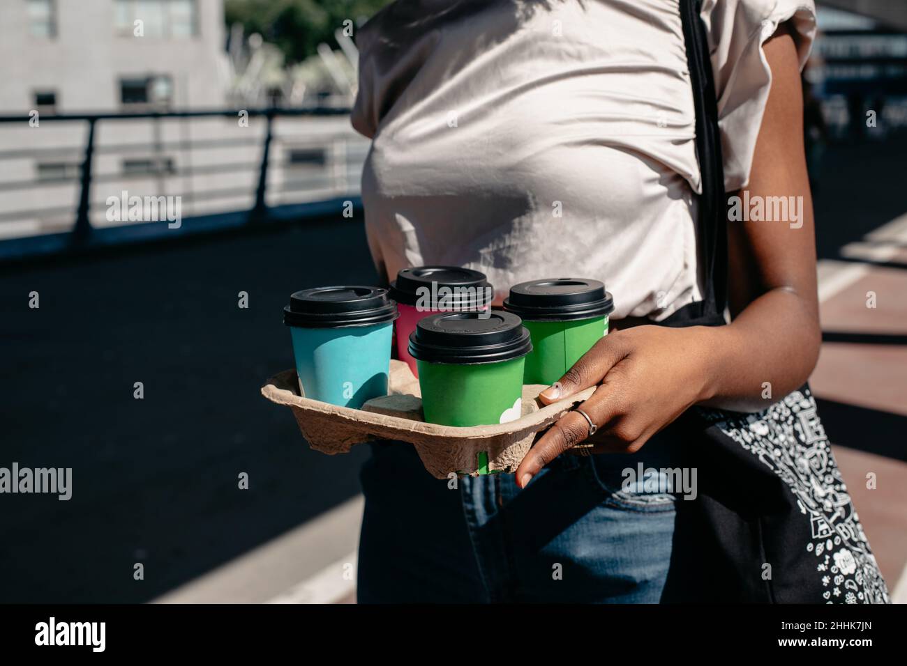 Crop anonyme afroamerikanische Frau in legerer Kleidung zu Fuß mit Papptablett mit Entsorgung Tassen mit Getränken zum Mitnehmen Stockfoto