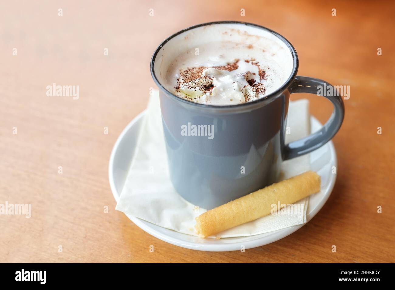 Heiße Trinkschokolade mit Schlagsahne und Kakaostreuseln serviert mit einem Cookie in einem blauen Becher auf einem Holztisch, Kopierraum, ausgewählter Fokus, schmal Stockfoto