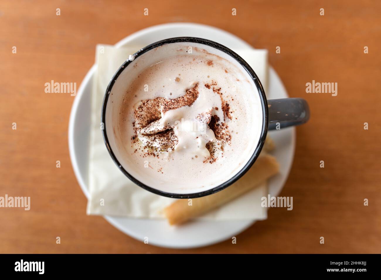 Heißer Schokoladendrink mit Schlagsahne und Kakaopulver, serviert mit einem Cookie in einem Becher auf einem Holztisch, Kopierraum, Blick von oben, selec Stockfoto