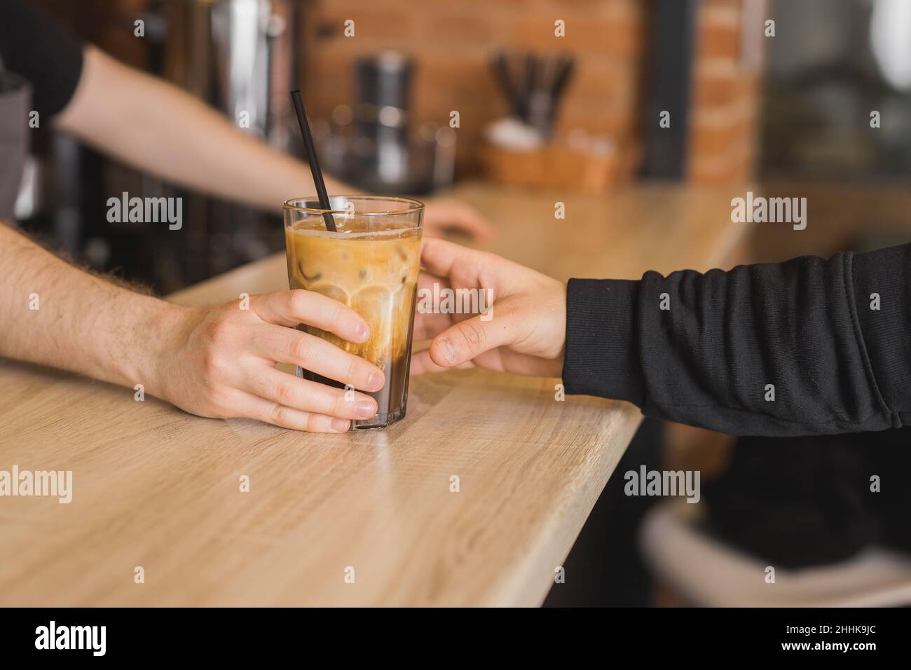Crop anonymer Barista, der dem Gast ein Glas Eismilchkaffee mit Stroh serviert, während er an der Theke im Café arbeitet Stockfoto