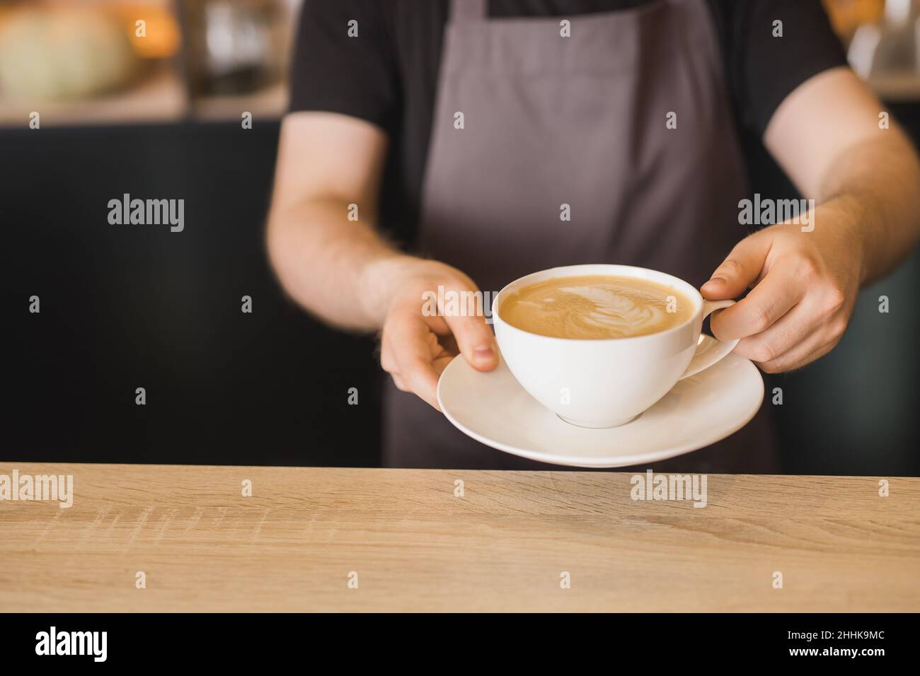 Schneiden Sie den männlichen Barista auf der Schürze zu, und servieren Sie eine Tasse Kaffee, während Sie am Bartisch im Café arbeiten Stockfoto