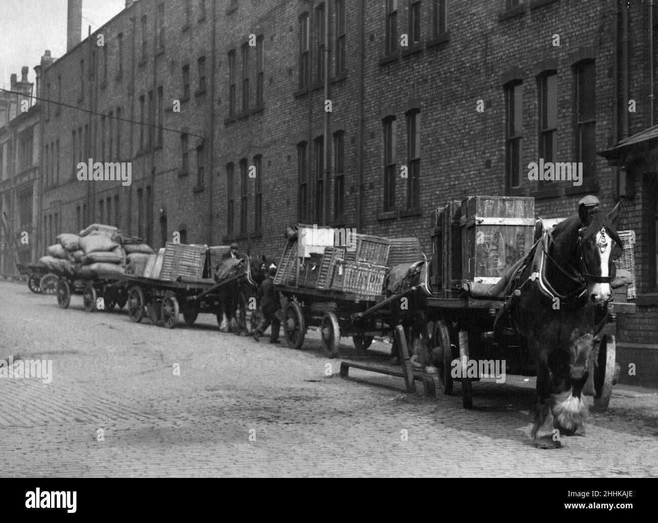 Schwere Pferde mit ihren Karren warten in dieser unbenannten Manchester Street darauf, ihre Lieferungen abzuladen. Ca. 1930 Stockfoto