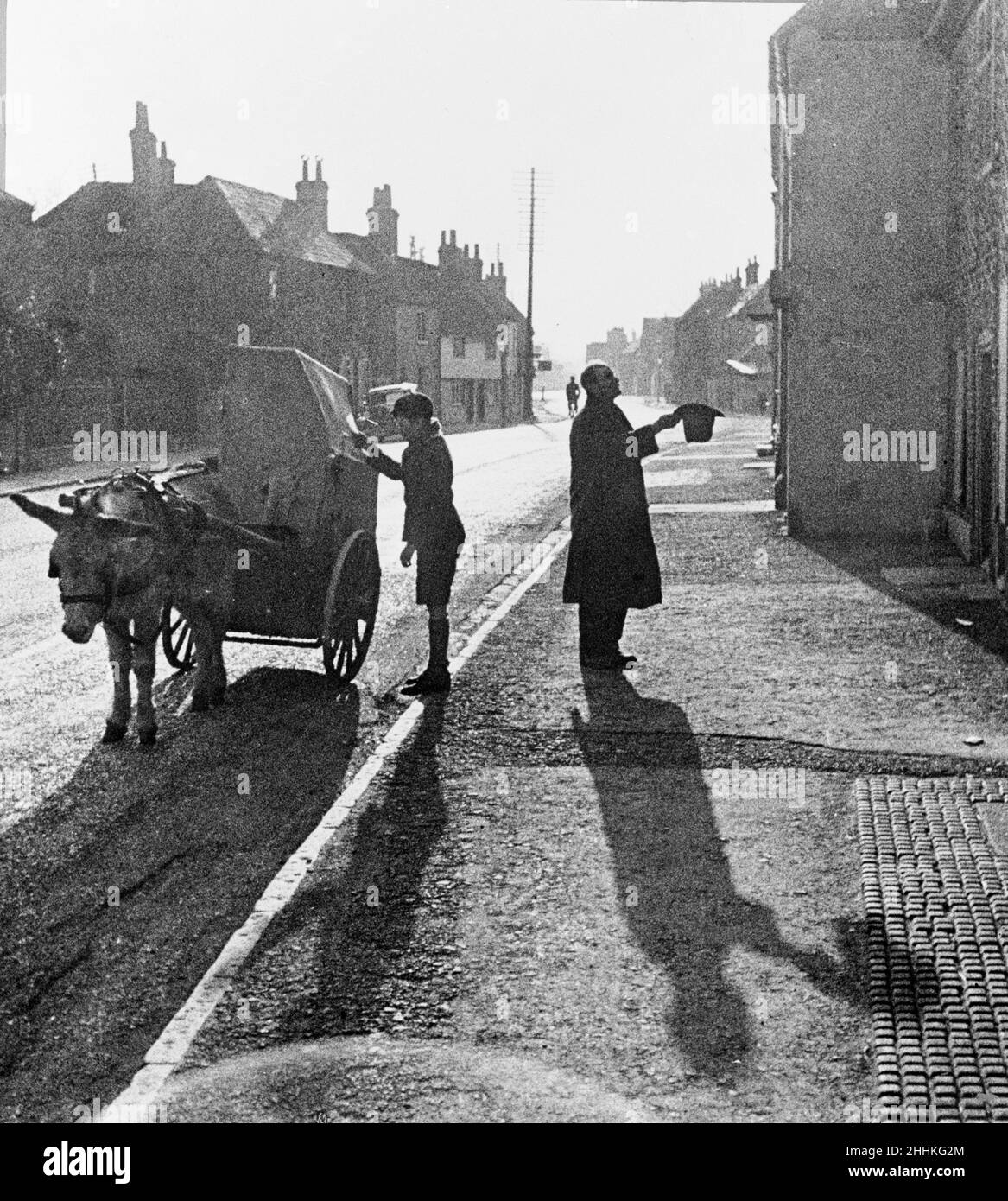 Ein Junge betreibt eine Tonnenorgel, die auf einem Esel und einem Wagen montiert ist, während der Vater des Jungen seinen Hut aushält. Ca. 1935 Stockfoto