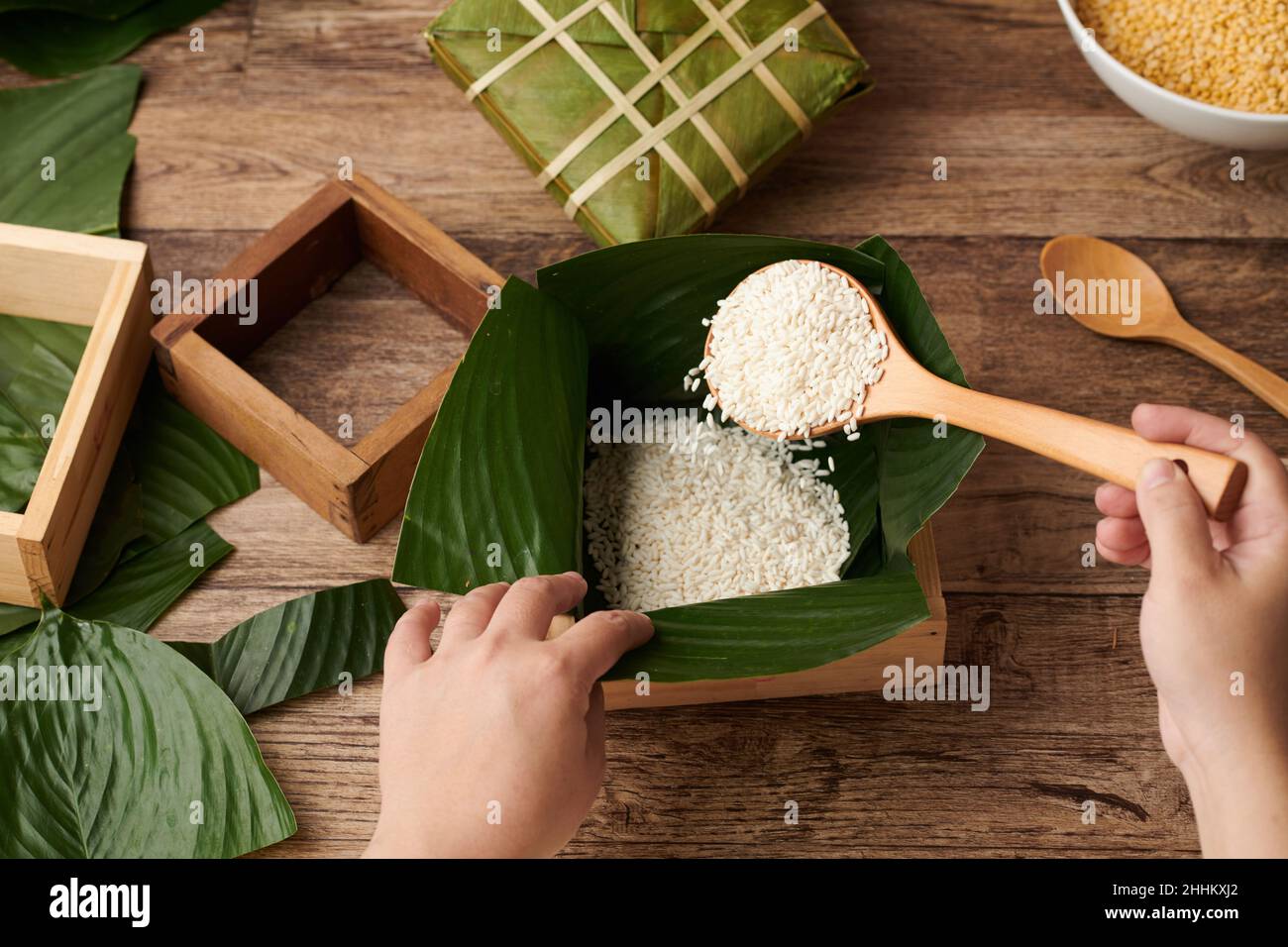 Hände einer Person, die Reis in Holzform mit Lotusblättern im Inneren einlegt, wenn Kuchen für die Tet-Feier gemacht wird Stockfoto