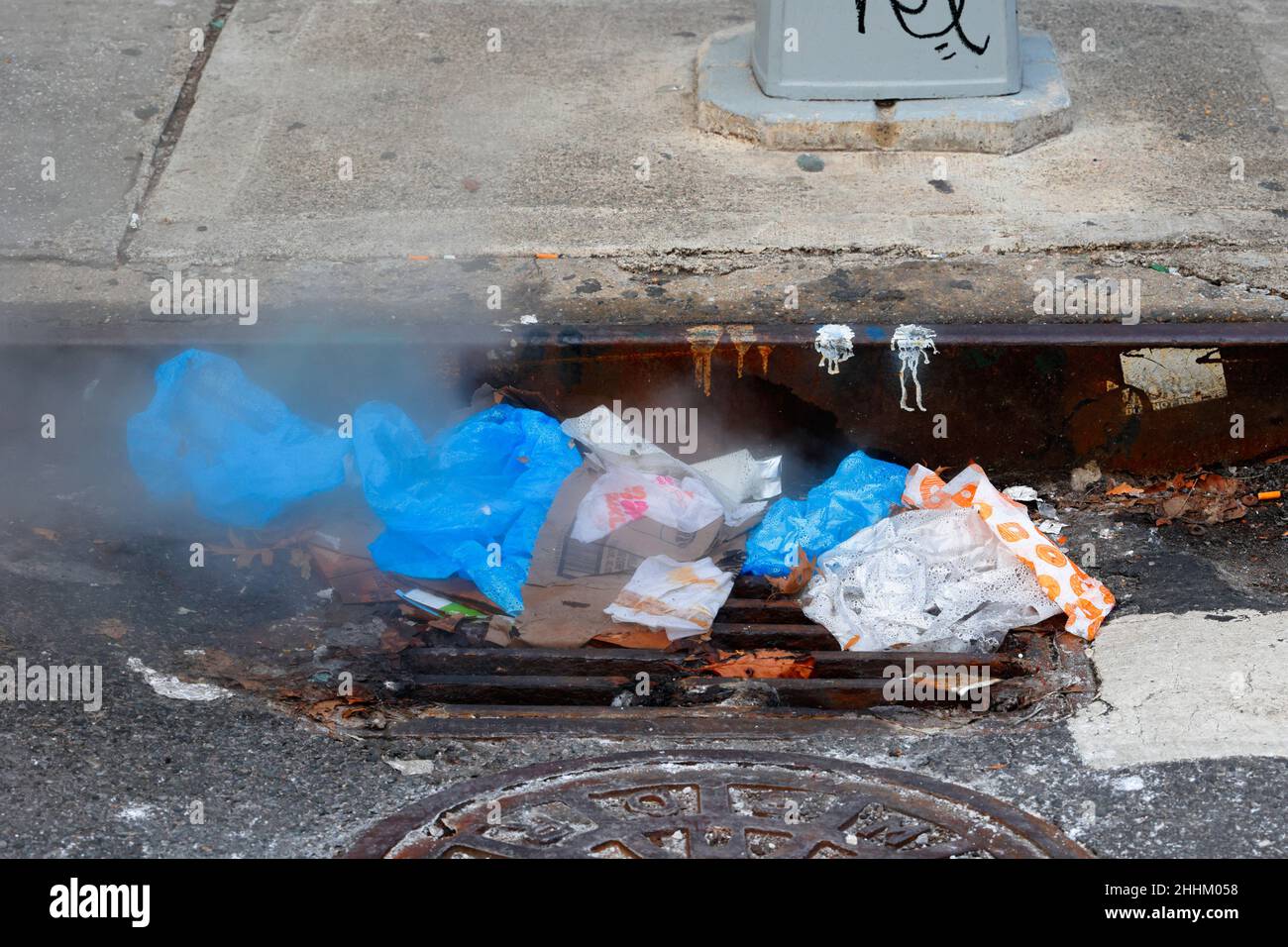 Ein dampfender Müllhaufen, der einen Sturmabfluss, ein Auffangbecken und ein Kanalrost in New York, NY, verstopft. Stockfoto