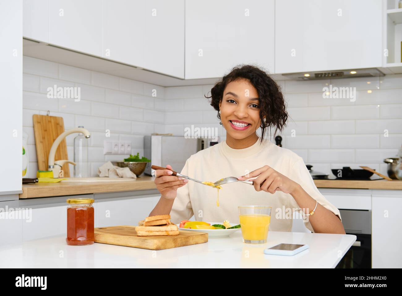 Lächelnde afroamerikanische Frau mit traditionellem Frühstück mit Spiegelei und frischem Gemüse zu Hause Stockfoto