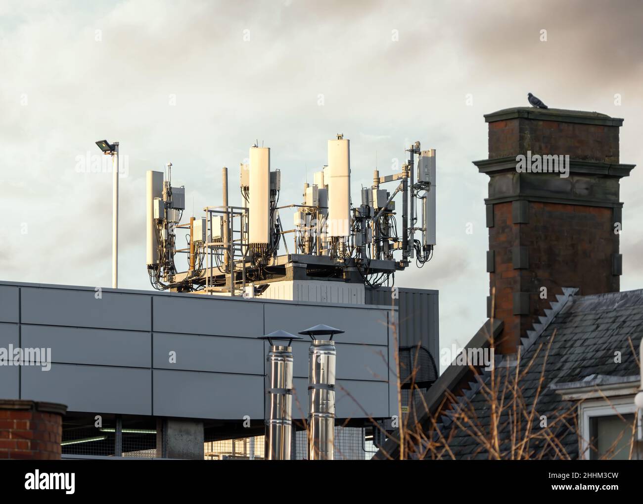 5G Mobilfunk-Funkmastsender bei Sonnenuntergang in Wohnstadt mit alten 4G und 3G Antennen ebenfalls angeschlossen. Gebäude unter hellem Himmel Stockfoto
