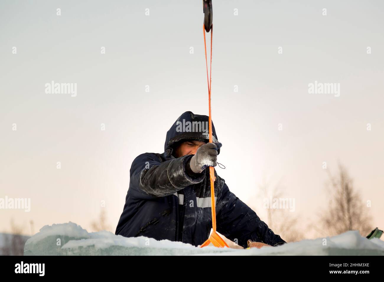 Slinger-Assembler in einer blauen Jacke mit Kapuze und schwarzem Hut lädt Eisblöcke Stockfoto