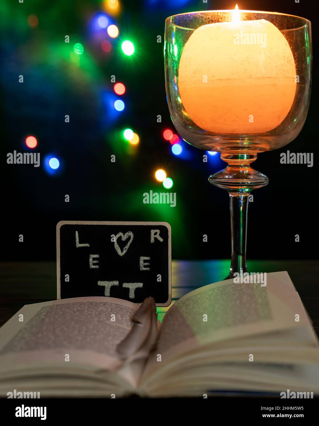 Aus einem Buch scheint ein Schiefer mit dem Wort „Brief“ zu kommen, daneben eine brennende Kerze und Bokeh-Lichter im Hintergrund Stockfoto