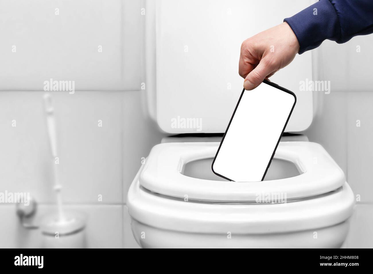 Die Hand wirft das Telefon mit einem leeren weißen Bildschirm in die Toilette oder den Mülleimer. Layout für Etiketten. Stockfoto