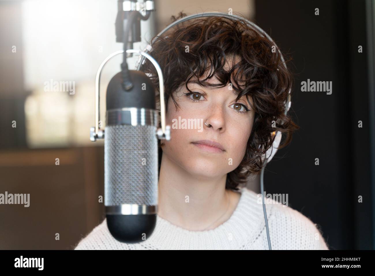 Eine junge Sängerin mit lockigen Haaren, die in einem echten Studio einen Song aufzeichnete Stockfoto