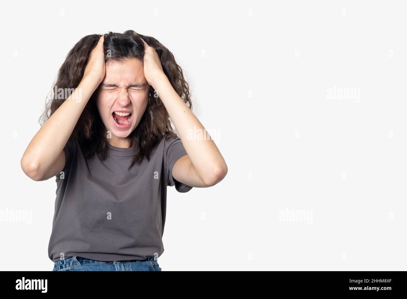 Aufgeregt schreiende Teenager Mädchen leiden Einsamkeit, ihren Kopf mit ihren Händen auf einem hellen Hintergrund halten, kopieren Raum. Konzept der psychischen Gesundheit. Stockfoto